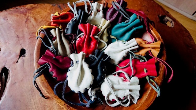 Een houten schaal vol kleurige leren buideltjes